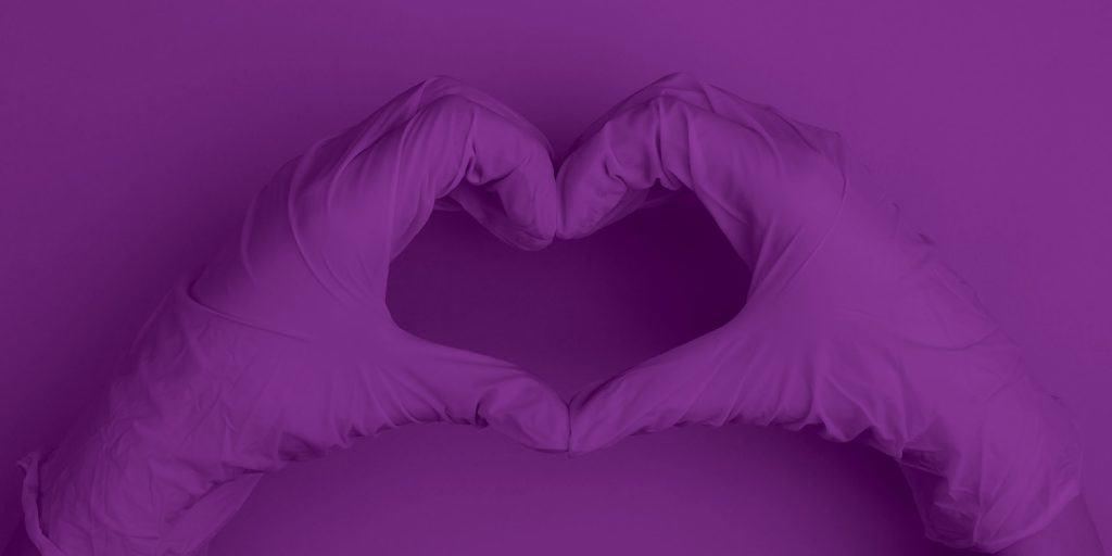 戴着手术手套的紫色手做出心脏的形状